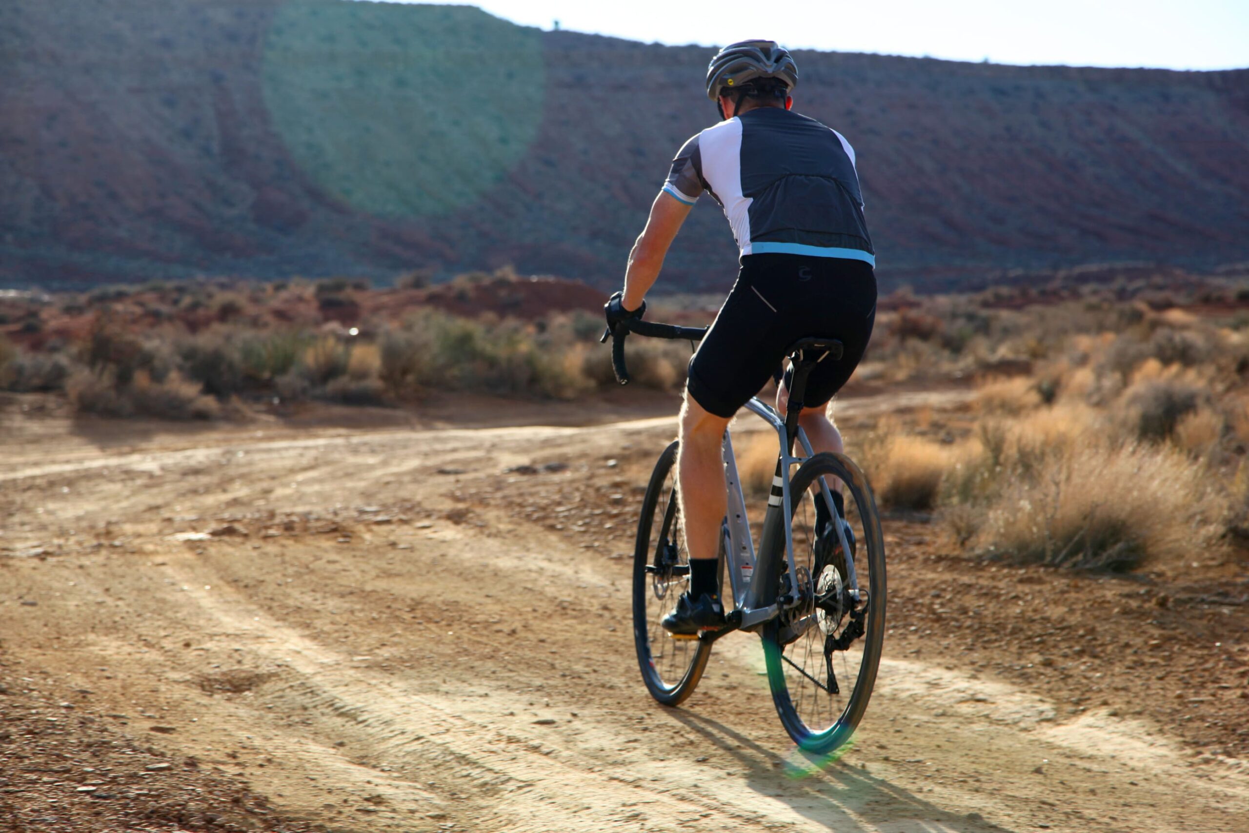Persoon fietst door de woestijn, op een onverharde weg met bergen op de achtergrond.