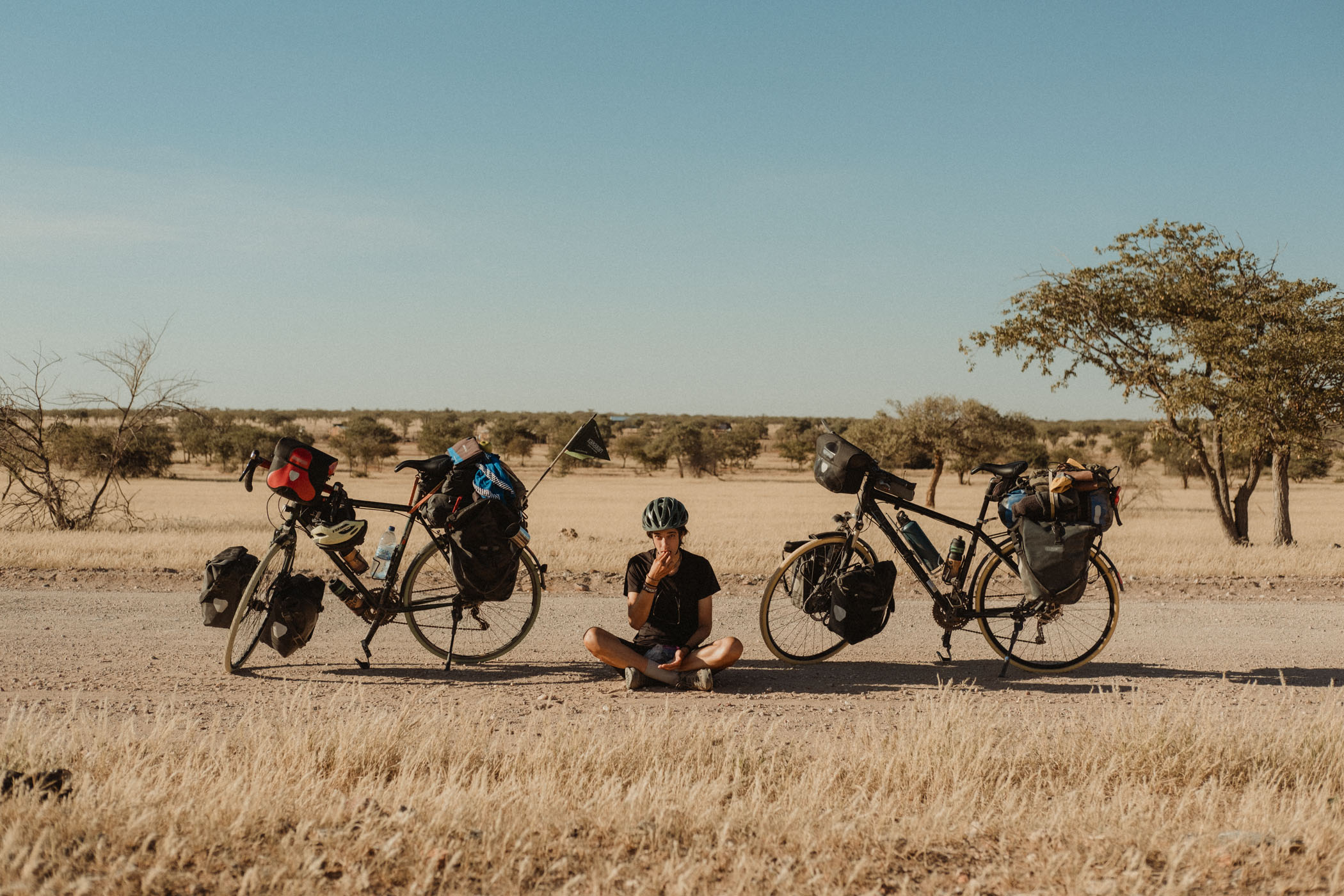 Elena assise en train de manger au milieu des deux vélos avec la savane en arrière-plan.