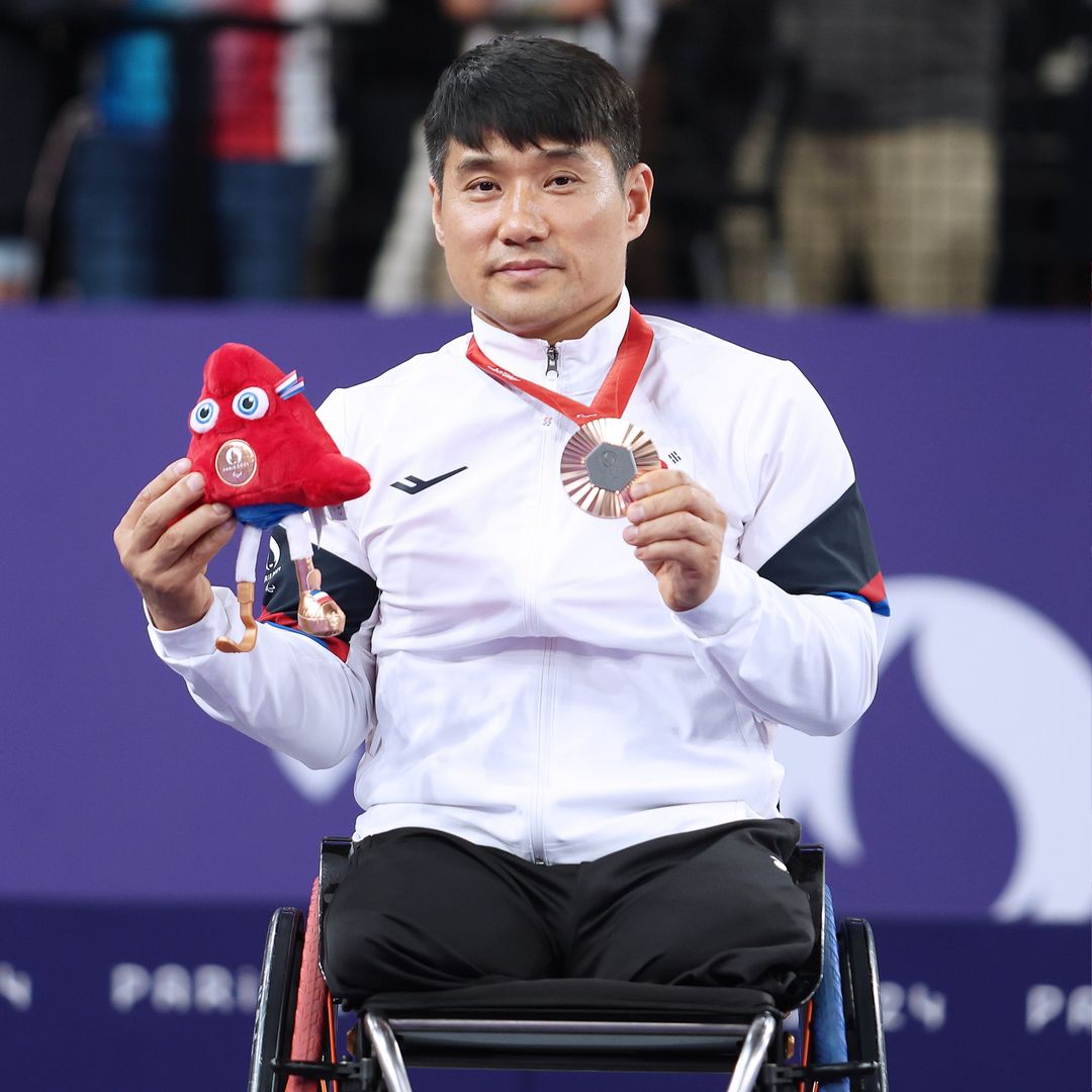 Athlete Kim Jungjun holding the gold medal with Tannus in his wheelchair.