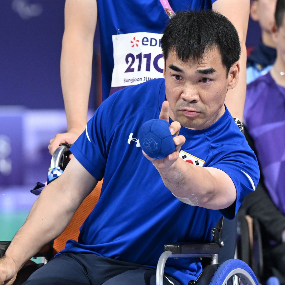 Der Sportler Jun Sungjung beim Boccia-Wettkampf mit den blauen Tannus-Rädern, den passenden Kugeln und der Uniform, die an seinem Rollstuhl angebracht sind.