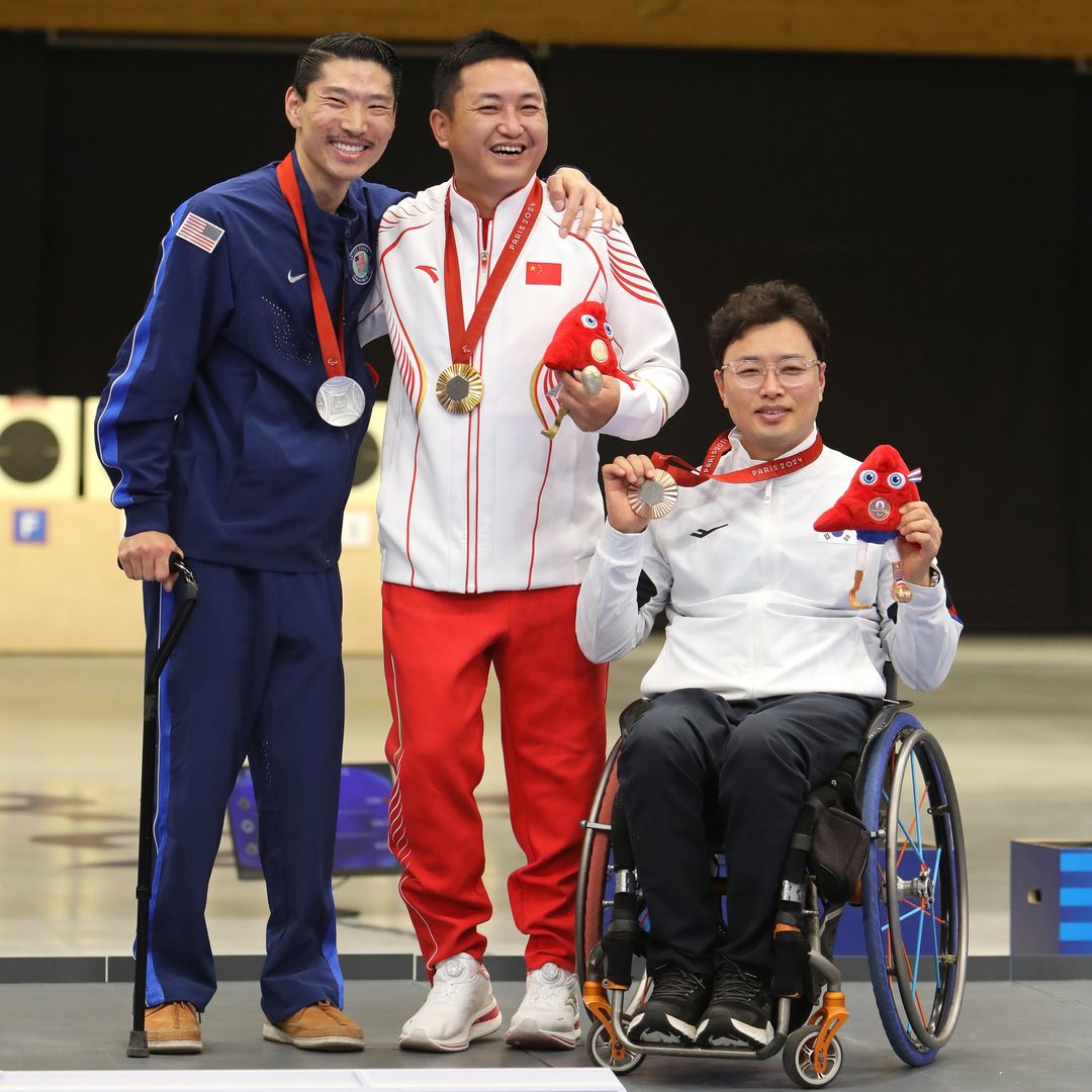 El atleta Kim Jugnam sujetando la medalla de bronce junto al medallista de plata y oro, con Tannus equipadas en su silla de ruedas