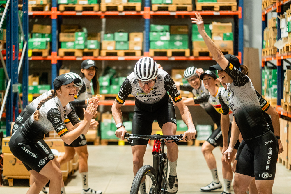 Riccardo Chierini sur son vélo dans les couloirs de l'entrepôt, entouré de tous ses collègues qui l'encouragent.